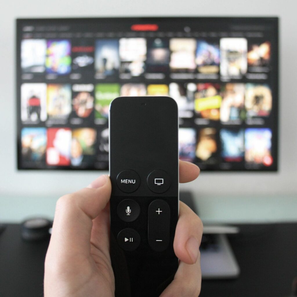 Image of a hand holding a remote control in front of a television